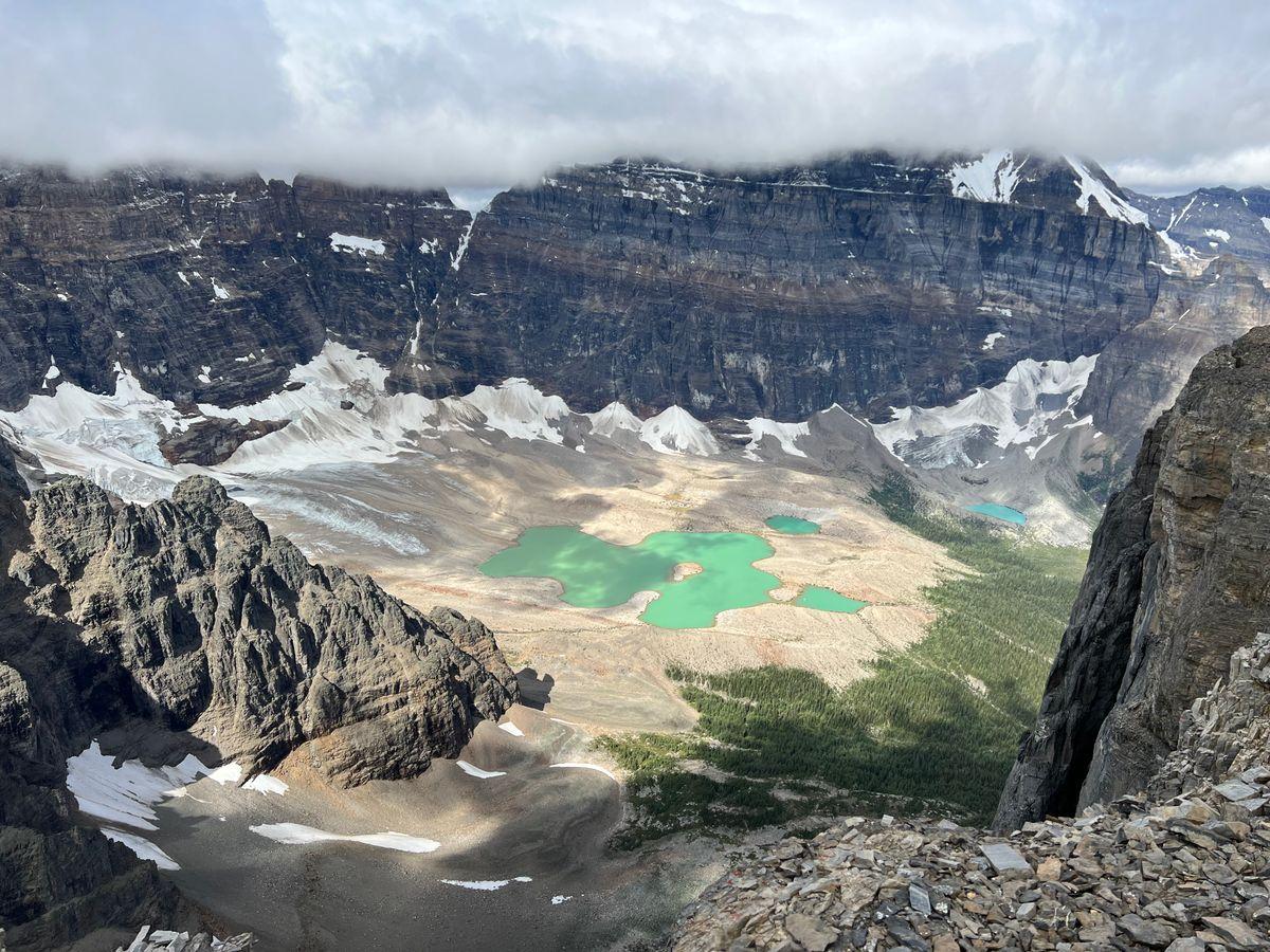 Turquoise glacial tarns on a high basin floor, ringed by cliffs and snowfields